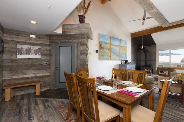 dining space featuring a wood stove, ceiling fan, dark hardwood / wood-style floors, and vaulted ceiling with beams