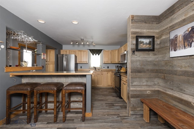 kitchen featuring wood walls, kitchen peninsula, dark wood-type flooring, appliances with stainless steel finishes, and light brown cabinets