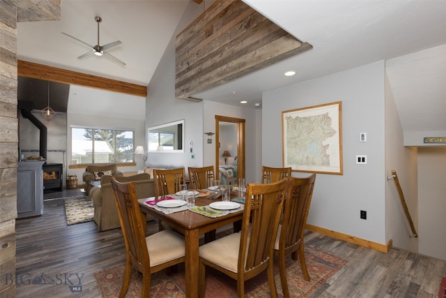 dining space with dark hardwood / wood-style floors, a wood stove, a large fireplace, high vaulted ceiling, and ceiling fan