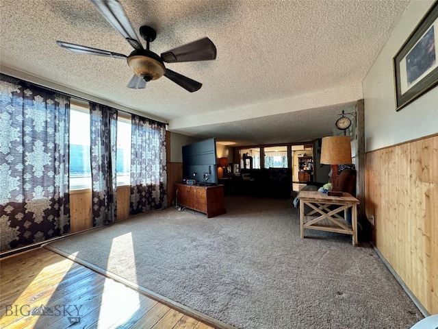 unfurnished living room featuring ceiling fan, wood-type flooring, a textured ceiling, and wooden walls