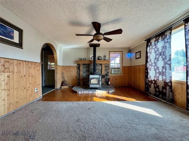 unfurnished living room featuring dark carpet, a textured ceiling, ceiling fan, cooling unit, and a wood stove