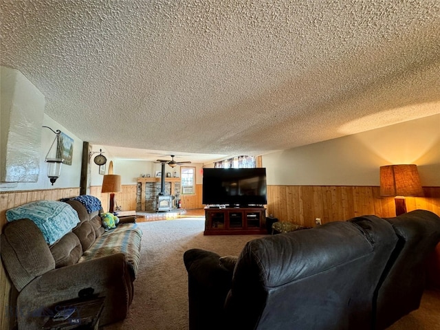 living room with a textured ceiling, carpet floors, a wood stove, and ceiling fan