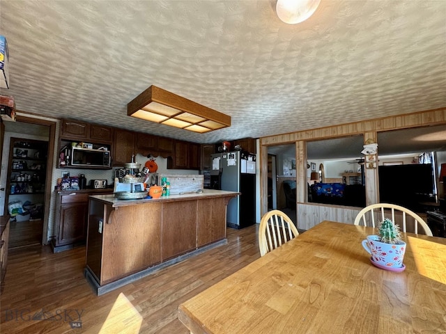 kitchen featuring black fridge, dark brown cabinets, a kitchen island, and dark wood-type flooring