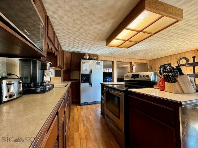 kitchen featuring wooden walls, light hardwood / wood-style flooring, stainless steel appliances, and a textured ceiling