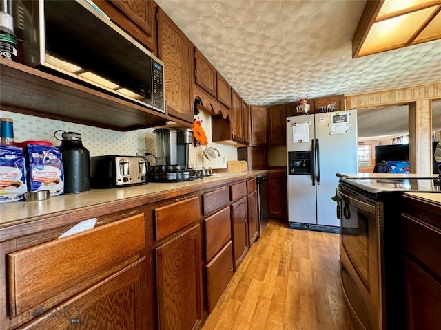 kitchen with appliances with stainless steel finishes, a textured ceiling, light hardwood / wood-style flooring, and sink