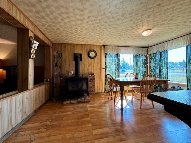 dining room featuring a textured ceiling, a wood stove, a wealth of natural light, and wood walls