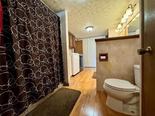 bathroom with a shower with shower curtain, a textured ceiling, hardwood / wood-style flooring, washing machine and clothes dryer, and toilet