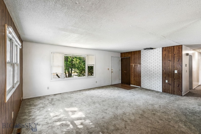 unfurnished room featuring a textured ceiling, wood walls, and carpet floors