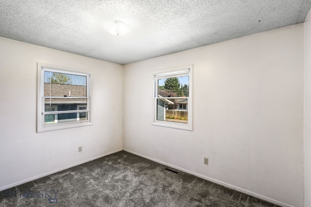 empty room featuring a textured ceiling and dark carpet