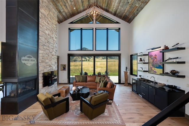 living room with a towering ceiling, a fireplace, a chandelier, light hardwood / wood-style floors, and wooden ceiling