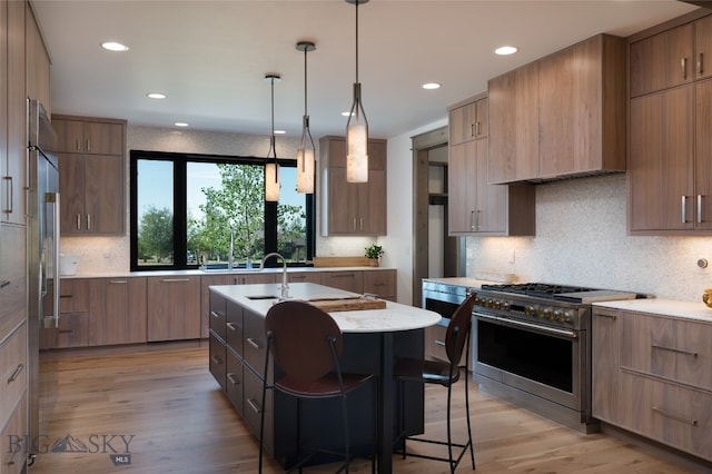 kitchen featuring light wood-type flooring, a kitchen breakfast bar, an island with sink, pendant lighting, and high end stove