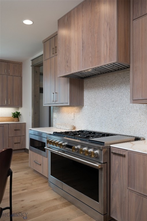 kitchen with light hardwood / wood-style flooring, stainless steel appliances, tasteful backsplash, light stone counters, and custom range hood