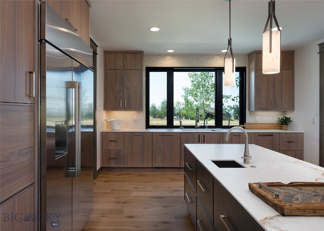 kitchen with high end fridge, sink, light stone counters, hanging light fixtures, and light hardwood / wood-style floors