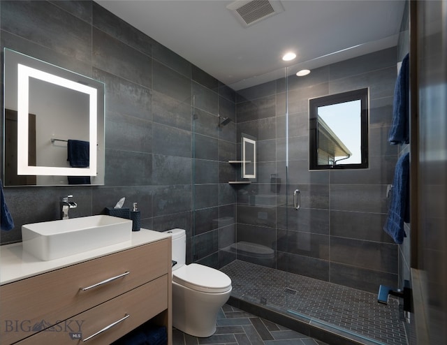 bathroom featuring tile patterned floors, toilet, a shower with shower door, tile walls, and vanity