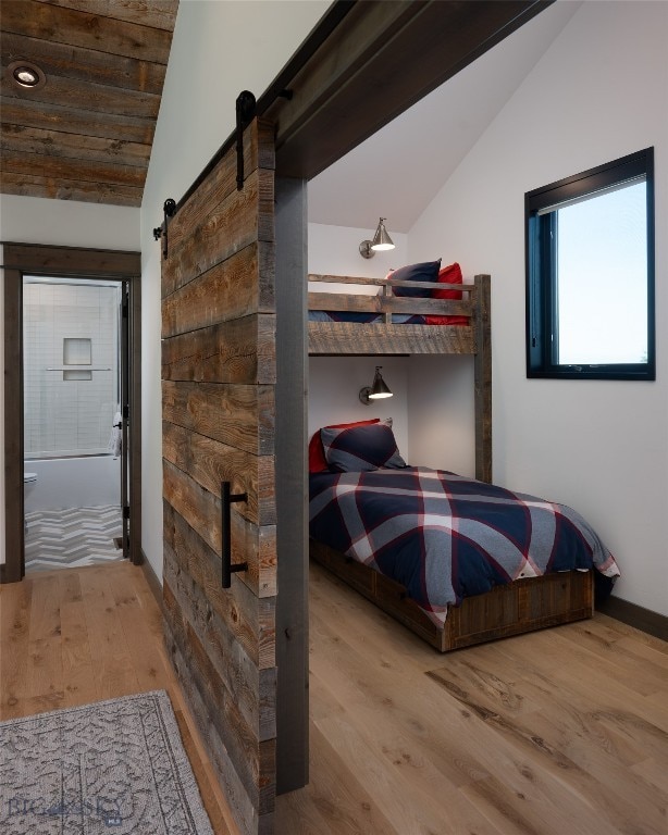 bedroom with hardwood / wood-style flooring, lofted ceiling, a barn door, and ensuite bathroom