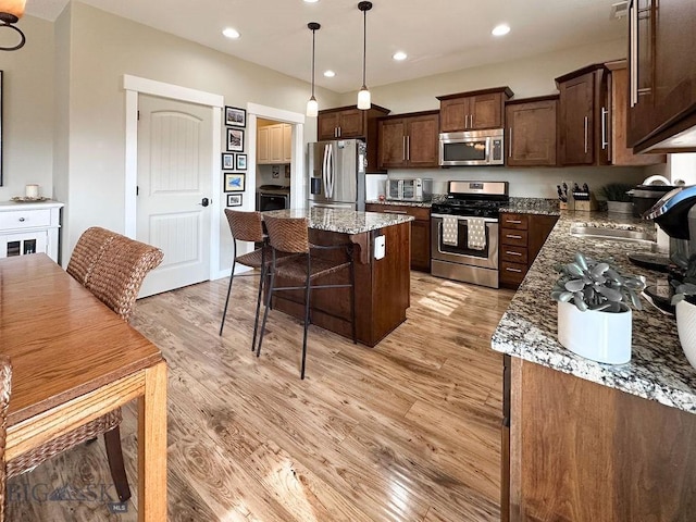 kitchen featuring a kitchen breakfast bar, a center island, dark brown cabinetry, appliances with stainless steel finishes, and light wood finished floors