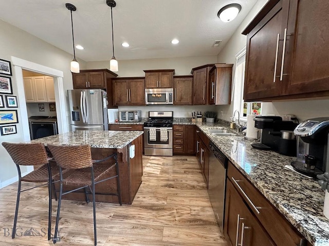 kitchen with a sink, stone countertops, a kitchen breakfast bar, appliances with stainless steel finishes, and light wood finished floors