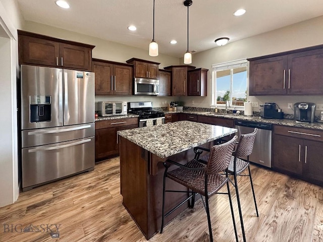 kitchen with stone counters, light wood finished floors, dark brown cabinets, and appliances with stainless steel finishes