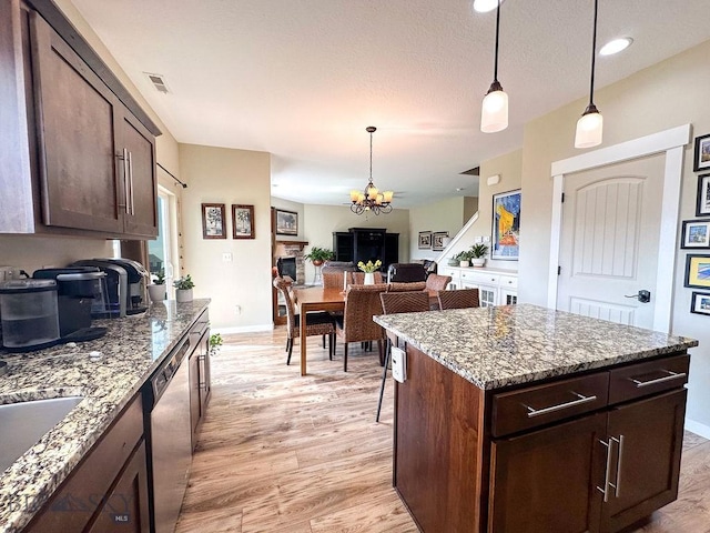 kitchen featuring light wood finished floors, stone countertops, hanging light fixtures, dark brown cabinetry, and dishwasher