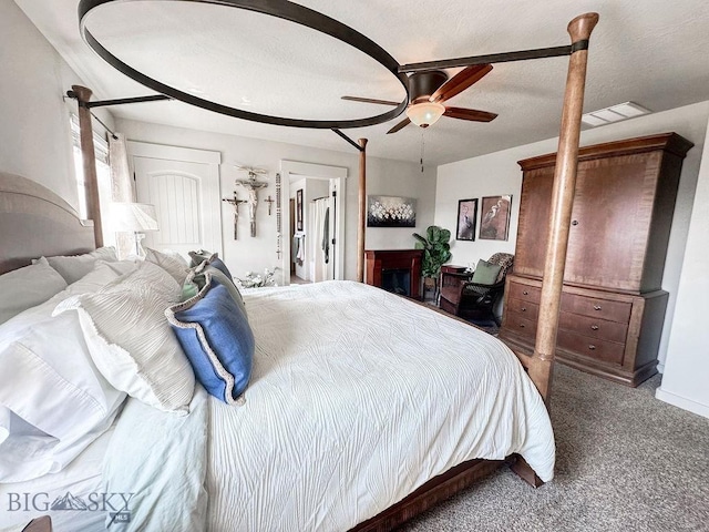 carpeted bedroom with ceiling fan, a fireplace, visible vents, and a textured ceiling