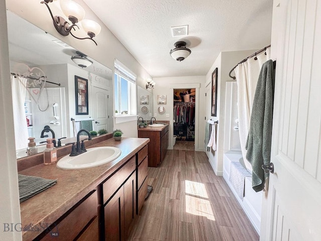 full bathroom featuring visible vents, a textured ceiling, wood finished floors, and a sink