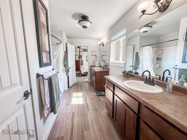 ensuite bathroom with wood finished floors, two vanities, a sink, ensuite bathroom, and a textured ceiling