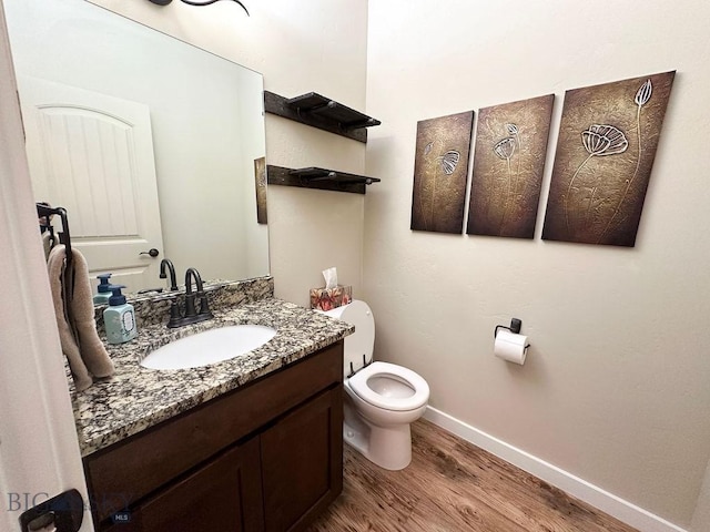 half bath featuring vanity, toilet, wood finished floors, and baseboards