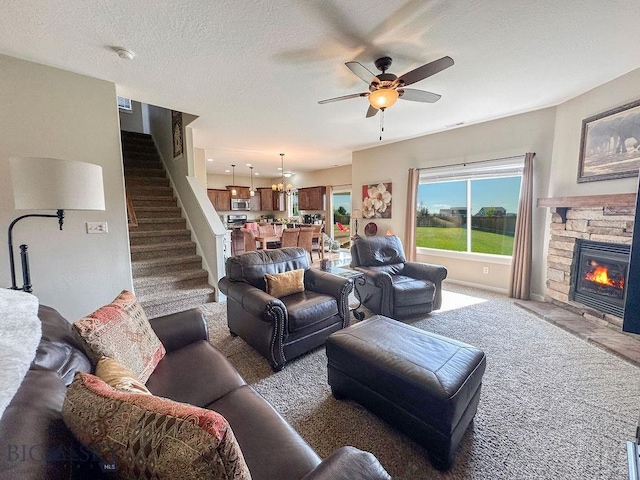 living room featuring a textured ceiling, carpet, a fireplace, ceiling fan, and stairs