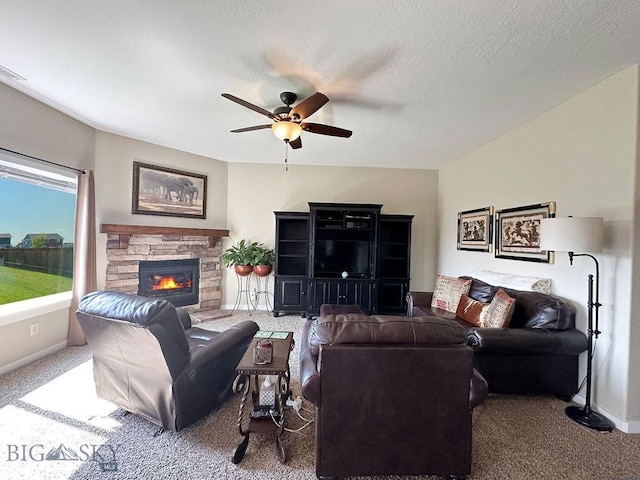 living room featuring baseboards, a stone fireplace, carpet flooring, a textured ceiling, and a ceiling fan