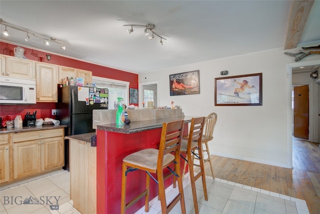 kitchen with a kitchen island, a kitchen breakfast bar, light hardwood / wood-style flooring, light brown cabinets, and black refrigerator