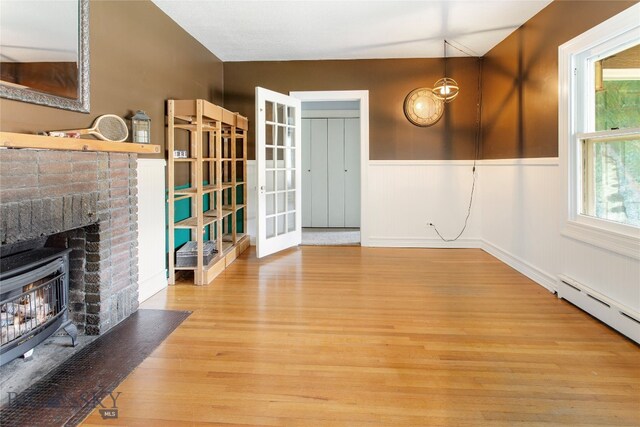 interior space featuring french doors, a brick fireplace, light hardwood / wood-style flooring, lofted ceiling, and a baseboard radiator