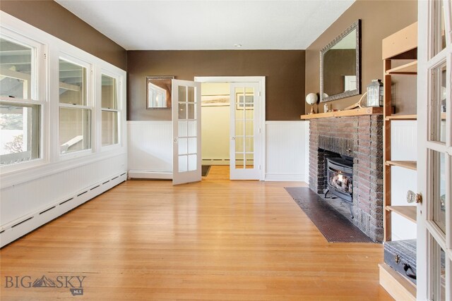 unfurnished living room with light wood-type flooring, a baseboard heating unit, a fireplace, and french doors