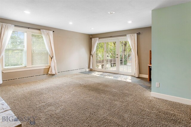 unfurnished room with a baseboard heating unit, light colored carpet, and a wealth of natural light