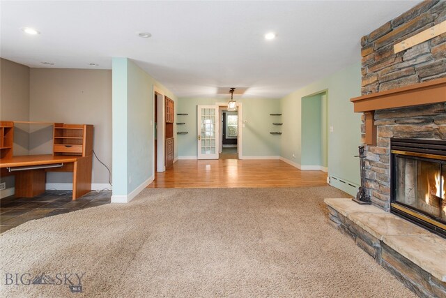 carpeted living room with a baseboard heating unit and a stone fireplace