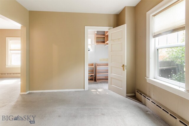 carpeted empty room featuring a baseboard heating unit and a healthy amount of sunlight