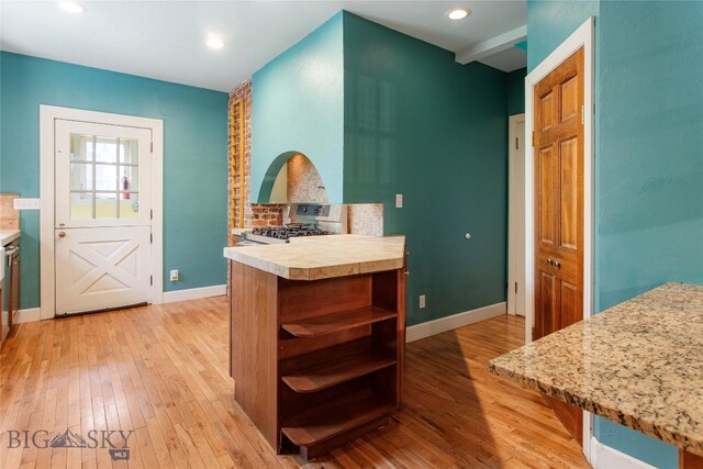 kitchen featuring light hardwood / wood-style flooring, kitchen peninsula, beam ceiling, and gas stove