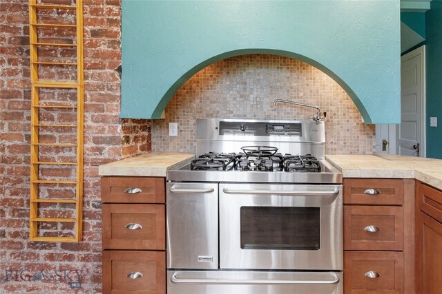 kitchen with stainless steel range with gas cooktop, decorative backsplash, and brick wall