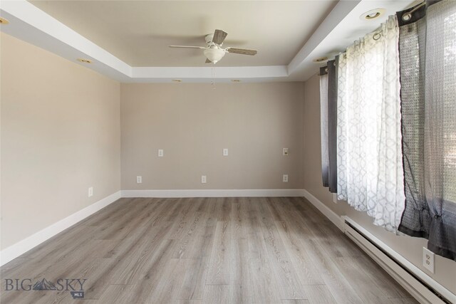 empty room featuring a healthy amount of sunlight, a baseboard radiator, light hardwood / wood-style floors, and ceiling fan