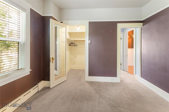 unfurnished bedroom featuring a baseboard radiator, a walk in closet, a closet, and multiple windows