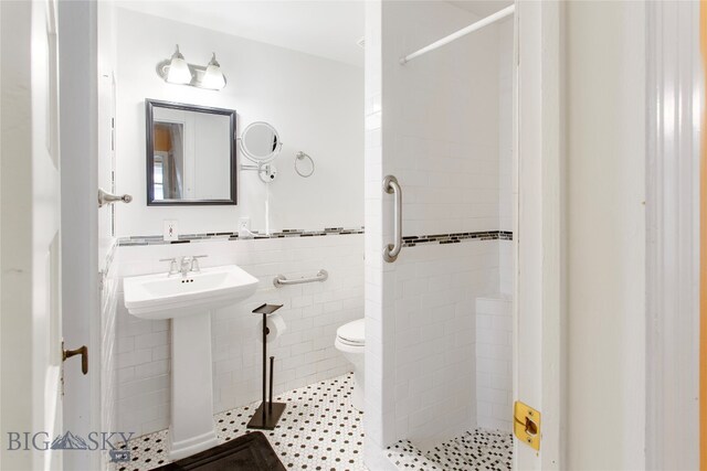 bathroom featuring toilet, tile patterned floors, tiled shower, sink, and tile walls