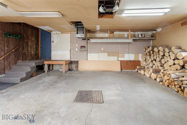 garage with a garage door opener, heating unit, and wood walls