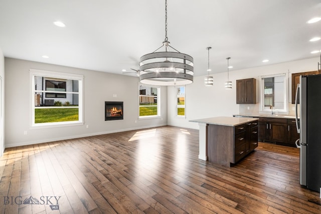 kitchen featuring a kitchen island, decorative light fixtures, dark brown cabinets, dark hardwood / wood-style flooring, and stainless steel refrigerator