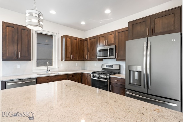 kitchen featuring light stone counters, hanging light fixtures, stainless steel appliances, and sink