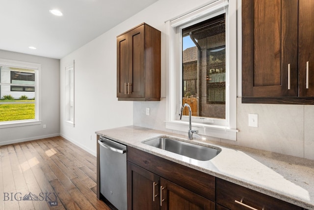 kitchen with light stone countertops, sink, wood-type flooring, dark brown cabinetry, and stainless steel dishwasher