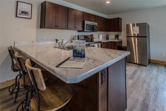 kitchen featuring kitchen peninsula, a breakfast bar area, appliances with stainless steel finishes, and light hardwood / wood-style floors