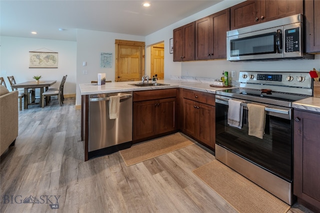 kitchen featuring stainless steel appliances, sink, light wood-type flooring, and kitchen peninsula