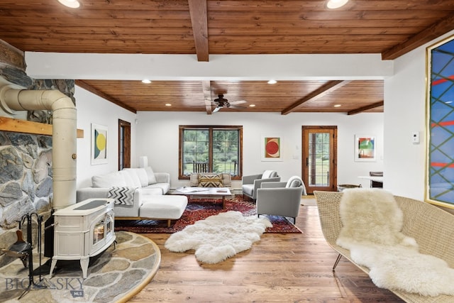 living room featuring ceiling fan, beam ceiling, hardwood / wood-style flooring, wooden ceiling, and a wood stove