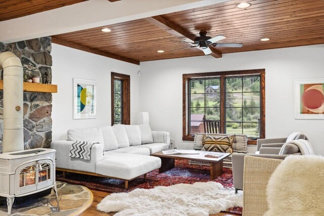 living room featuring ceiling fan, beam ceiling, hardwood / wood-style flooring, wooden ceiling, and a wood stove