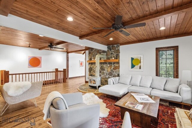 living room with beam ceiling, light hardwood / wood-style floors, a wood stove, and wood ceiling