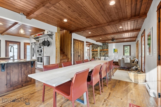 dining area with beam ceiling, sink, wooden ceiling, a stone fireplace, and light wood-type flooring